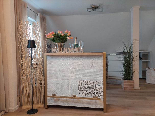 Heller Raum mit einer Bar, Blumen, Gläsern und einer Stehlampe.